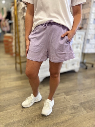 Model wearing light purple shorts and white sneakers in a store setting