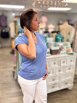 Woman in a blue shirt and white pants standing in a store with mannequins and products in the background.