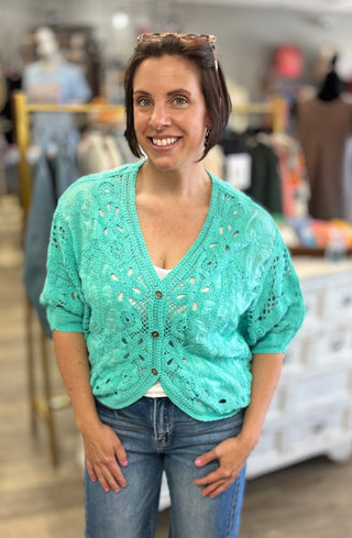 Woman wearing a short sleeve mint crocheted cardigan in a store setting