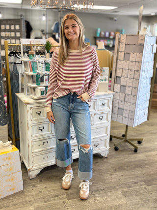 Model wearing a cream and burgundy striped sweater with jeans and sneakers.