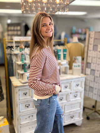 Model wearing a cream and burgundy striped sweater with jeans.