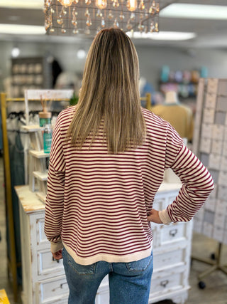 Model wearing a cream and burgundy striped sweater with jeans.