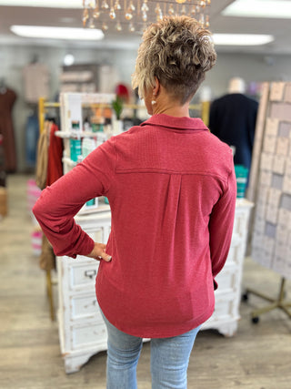 Back view of a heather red button-up top showing the back yoke, center pleat, long sleeves, and curved hem.