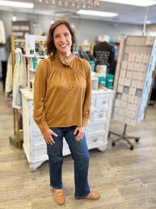 Model wearing a camel colored suede long sleeve top with snap and ruffle details, jeans, and loafers.