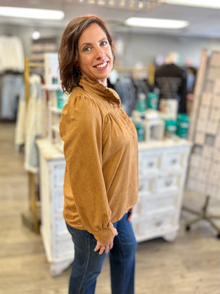 Model wearing a camel colored suede long sleeve top with snap and ruffle details.