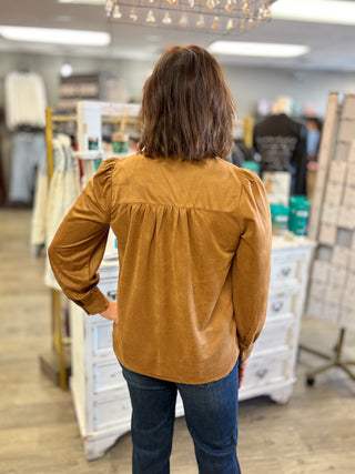 Model wearing a camel colored suede long sleeve with jeans.