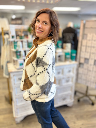 Model wearing a cream, grey, and camel argyle printed cardigan with jeans.