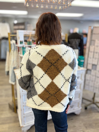Model wearing a cream, grey, and camel argyle printed cardigan and jeans.