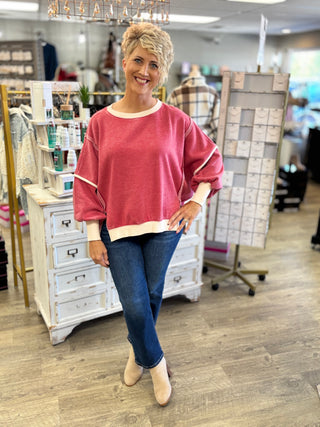 Full-length view of a model wearing a dark red and cream fleece sweatshirt with dark-wash jeans and beige ankle boots.