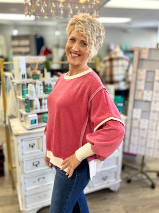 Side view of a dark red fleece sweatshirt showing dropped shoulders, roomy sleeves, cream trim, and a split hem.