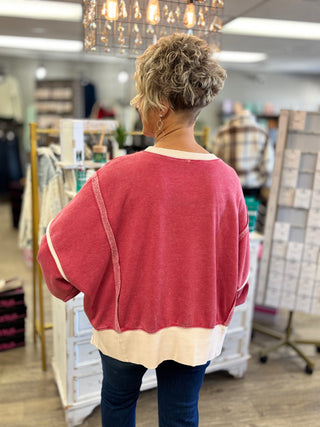 Back view of a dark red fleece sweatshirt with exposed seams, dropped shoulders, and a wide cream hem.