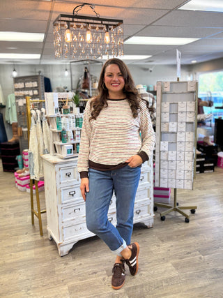 Full outfit featuring a cream striped top with brown trim, cuffed blue jeans and brown sneakers.