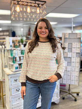 Front view of a cream striped long-sleeve top with brown neckline, cuffs and hem, worn with blue jeans.