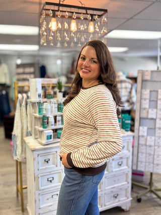 Side view of a cream multicolor striped top with long sleeves and brown trim, paired with blue jeans.