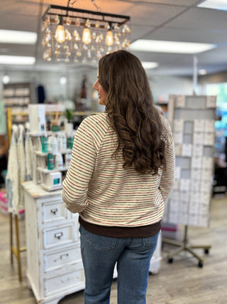 Back view of a cream horizontal-striped long-sleeve top with a brown banded hem, worn with blue jeans.